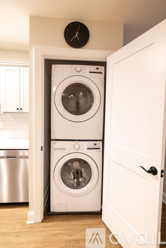 A white door opens to a laundry room with a washer and dryer stacked on top of each other.