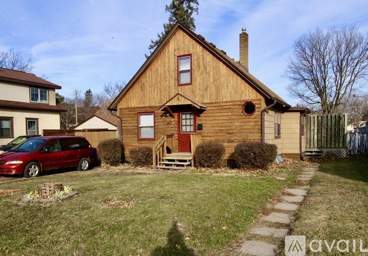 A red van is parked in front of a wooden house.