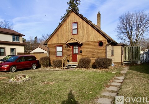 A red van is parked in front of a wooden house.