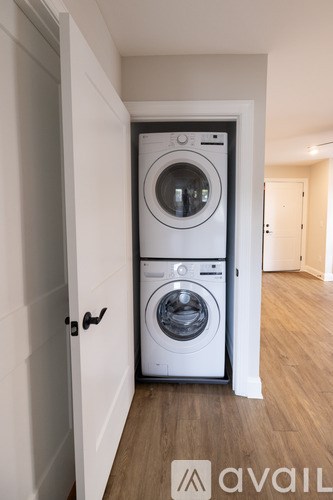 A white washing machine is in a small, white-walled laundry room.