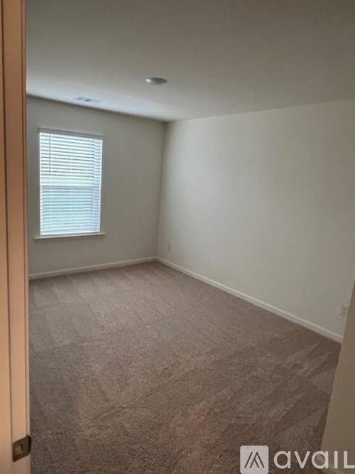 A room with carpeted floor and a window with blinds.
