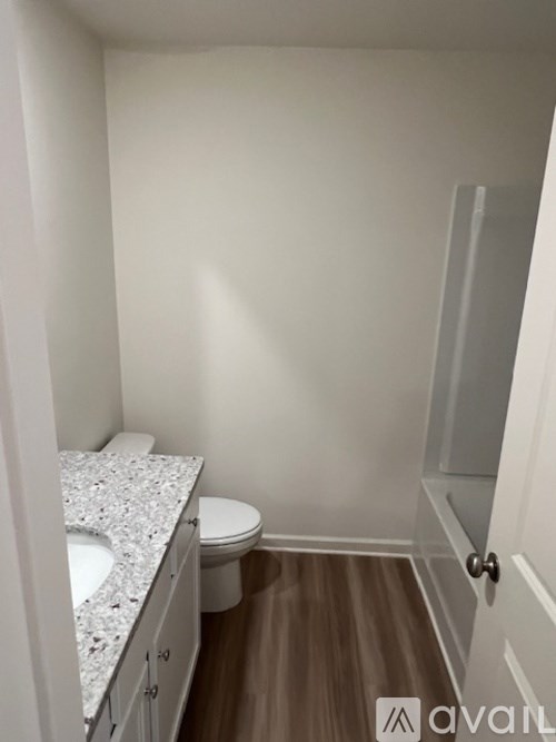 A bathroom with a toilet, sink, and wooden floor.