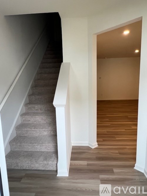 A staircase with a carpeted runner and white risers leads to a room with wooden flooring.