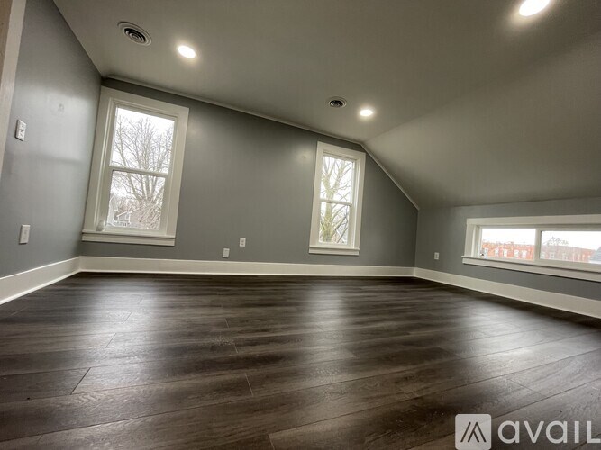 A spacious room with wood flooring and two windows.