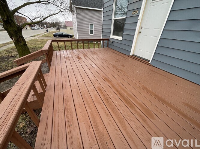 A wooden deck with a bench and a tree in front of a house.