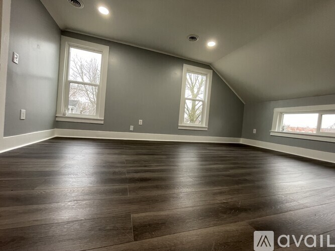 A spacious room with wood flooring and two windows.