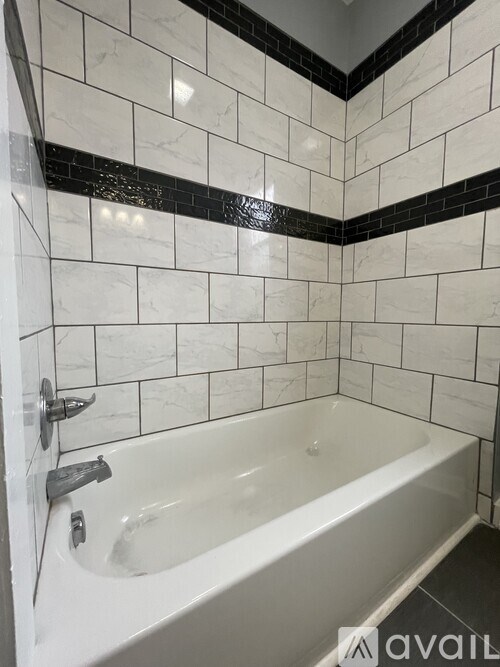 A white bathtub with a silver faucet is in a bathroom with black and white tiles.
