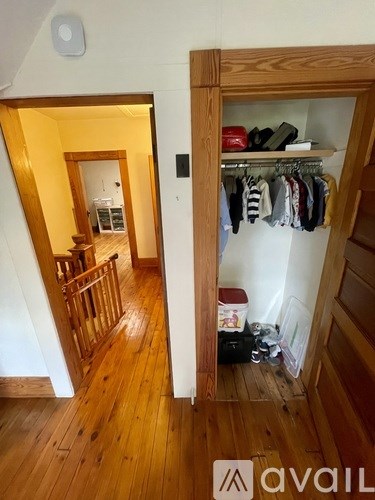 A hallway with a wooden floor and a white wall with a closet on the right.