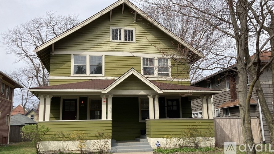 A green house with a porch and a tree in front.