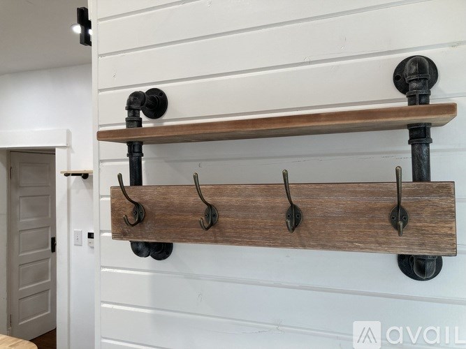 A wooden coat rack with five hooks is mounted on a white wall.