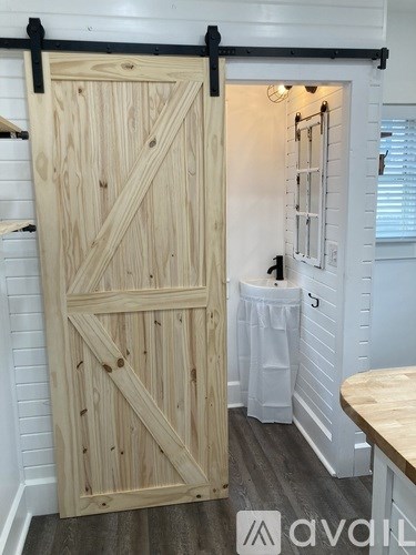 A wooden door with a black handle is open to a white bathroom.