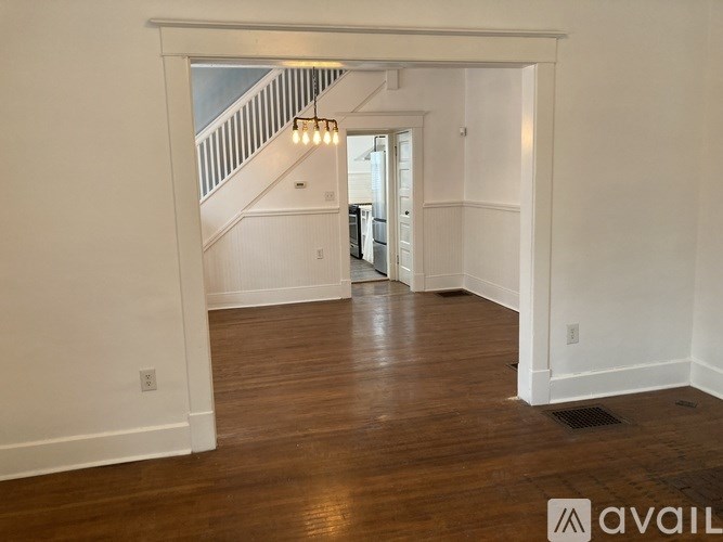 A spacious room with wooden floors and a staircase in the background.