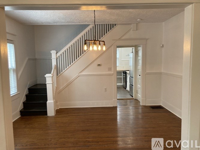 A spacious room with wooden floors and a staircase with white railings.