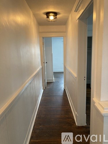 A long hallway with a light on the ceiling and a door at the end.