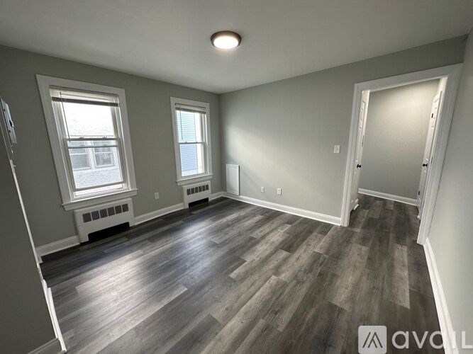 A room with wood flooring and two windows.