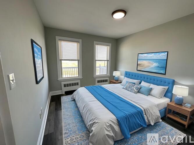A bedroom with a blue bedspread and a painting of a beach on the wall.