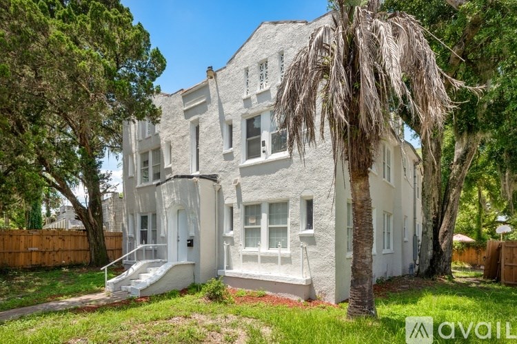 A white two-story house with a front porch and a tree in front.