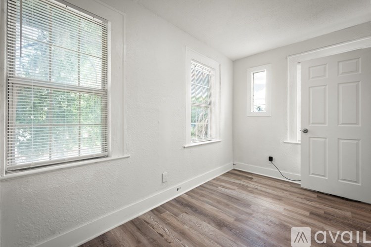 A room with a white door, a window with blinds, and a wooden floor.