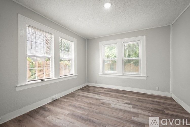 A room with wooden flooring and two windows.