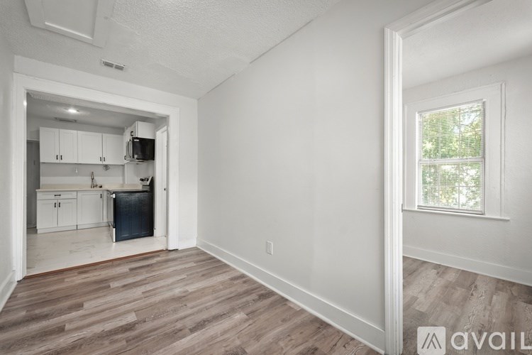A room with a window and a kitchen area in the background.