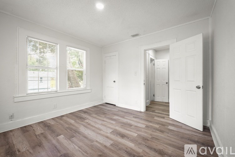 A room with wooden flooring and white walls, with a door leading to another room.