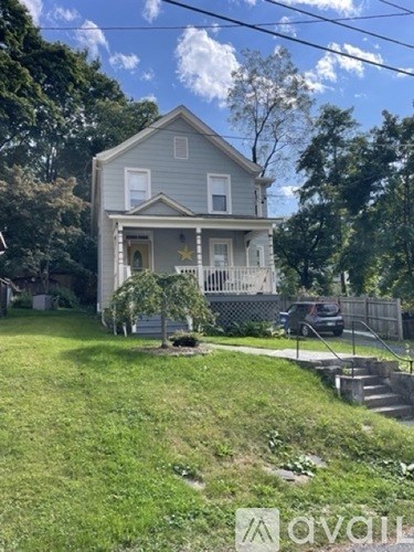 A two-story house with a front porch and a car parked in the driveway.