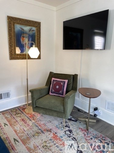 A living room with a green chair, a small table, and a painting on the wall.
