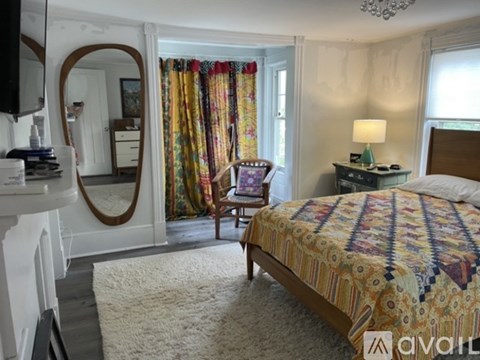 A bedroom with a large bed and a chair in front of a window with curtains.