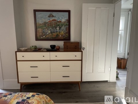 A painting hangs above a chest of drawers in a room.