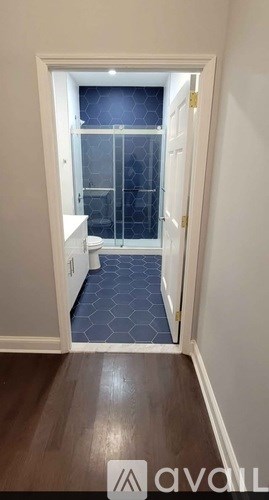 A hallway with a toilet and a glass door leading to a bathroom.