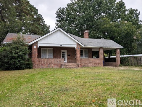 A house with a white roof and brick walls is surrounded by trees.
