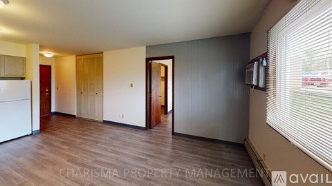 A spacious room with wooden floors and a white refrigerator on the left side.