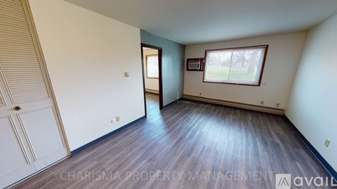 A spacious room with wooden flooring and a window with blinds.