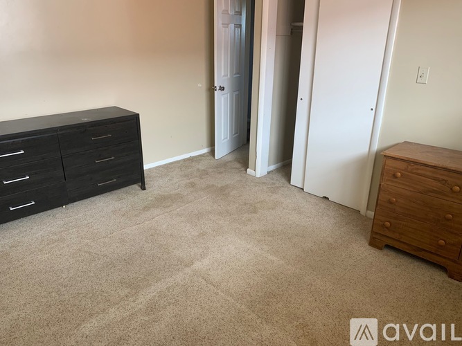 A room with a carpeted floor, a black dresser, and a wooden chest of drawers.