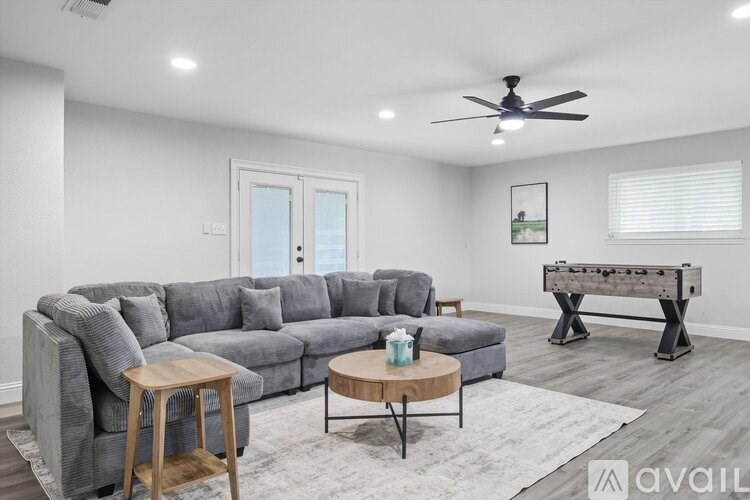 A living room with a grey couch, a wooden stool, a coffee table, and a pool table.