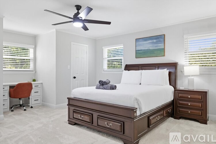 A bedroom with a large bed, a desk with a chair, and a ceiling fan.