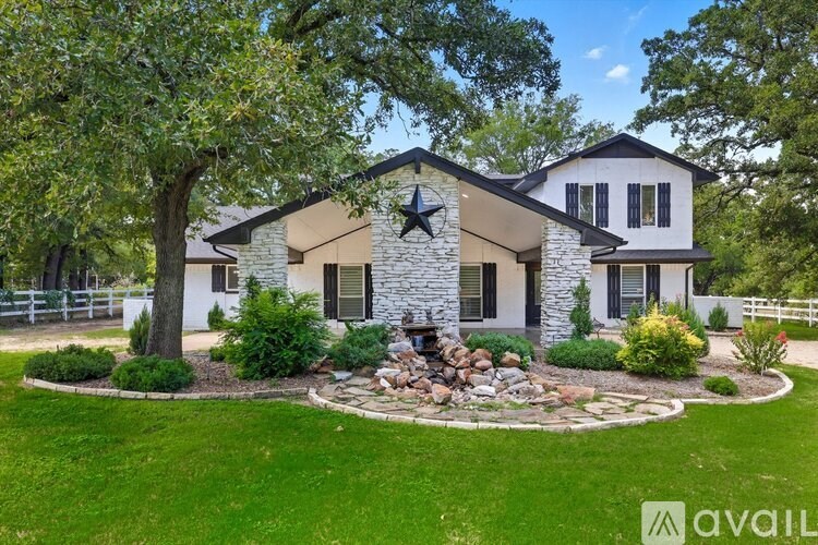 A house with a stone facade and a black star on the roof is surrounded by a well-manicured lawn and trees.