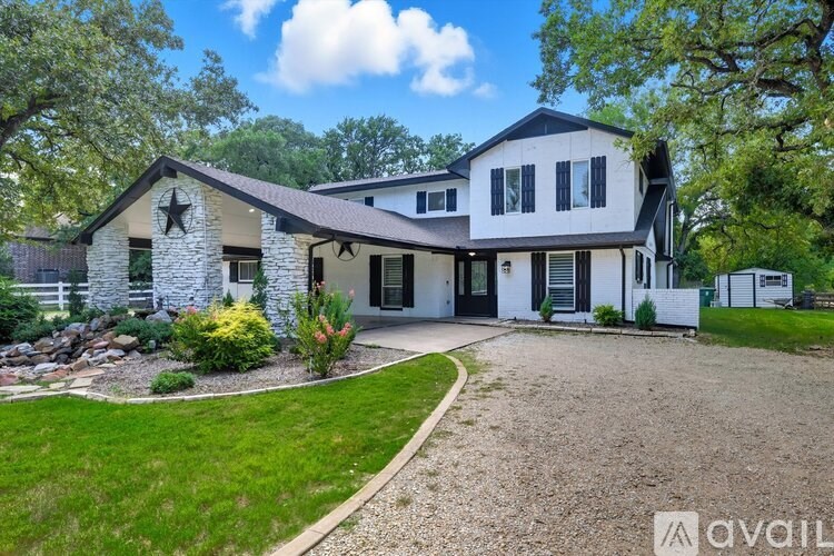 A house with a white exterior and a black roof is surrounded by greenery.