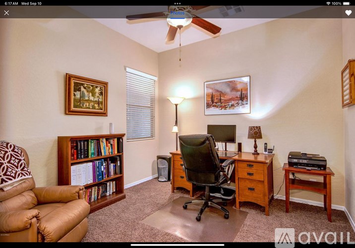 A room with a ceiling fan, a chair, a desk, and a bookshelf.