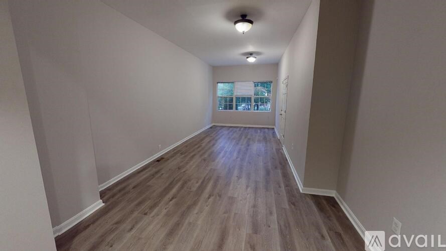 A long hallway with wood flooring and a window at the end.