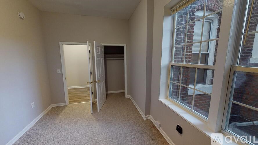 A room with a carpeted floor and a window showing a brick building outside.