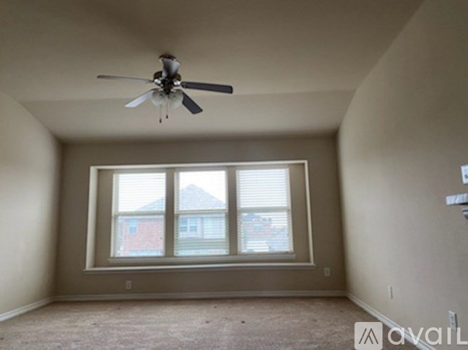 A room with a ceiling fan and a window overlooking a house.