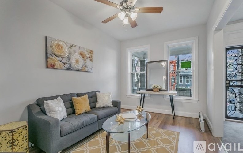 A living room with a grey couch, a glass table, and a painting on the wall.