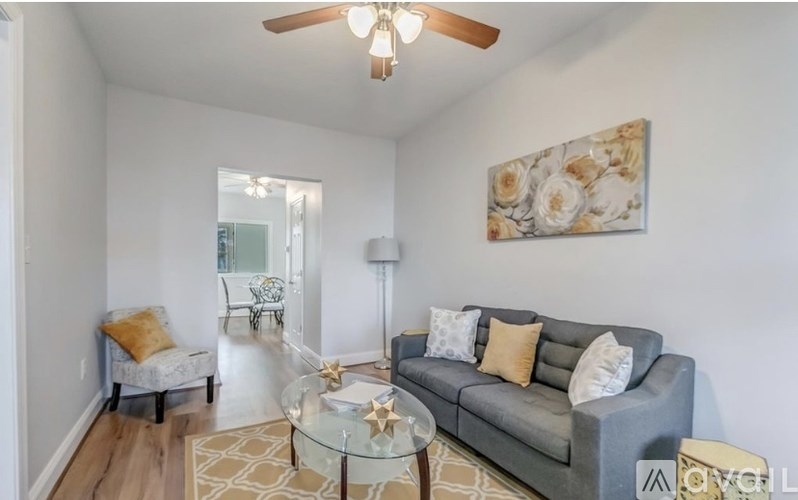 A living room with a grey couch, a glass table, and a painting on the wall.