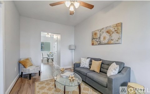 A living room with a grey couch, a glass table, and a painting on the wall.