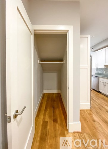 A hallway with a door on the left and a kitchen in the background.
