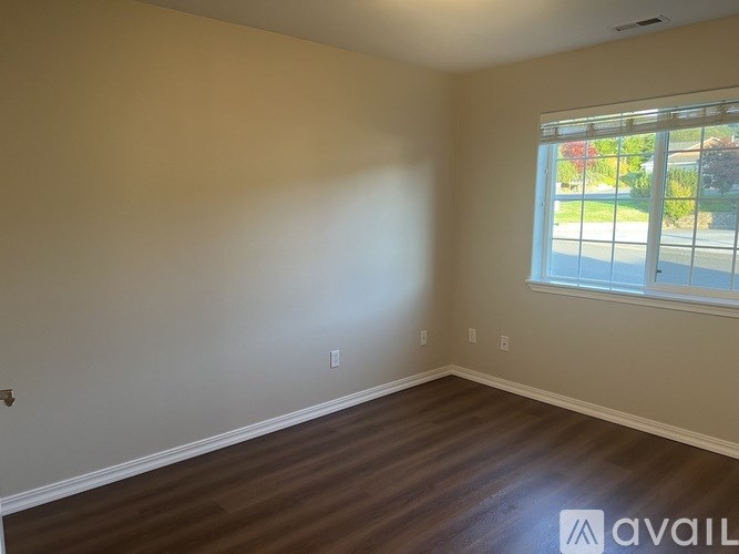 A room with wooden flooring and a window showing a view of a street.