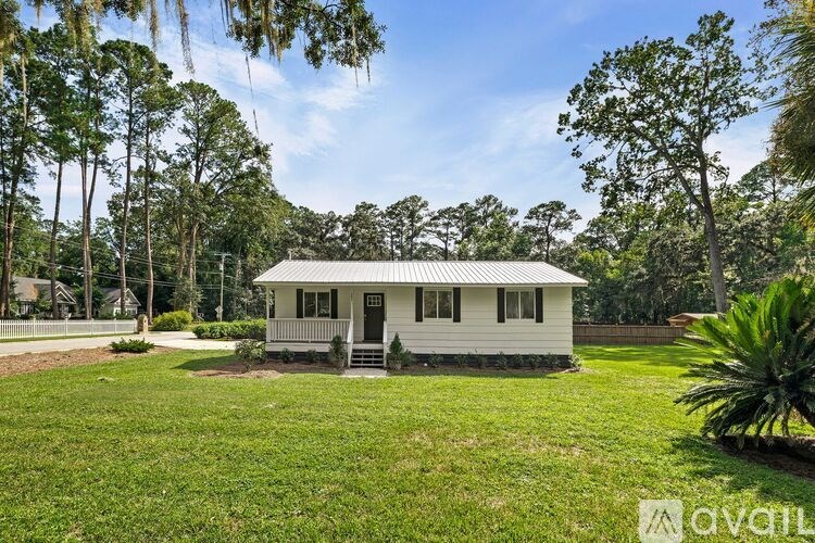 A small white house with a porch is surrounded by greenery and trees.