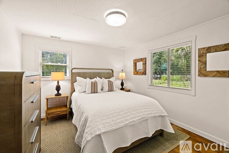 A bedroom with a large bed, a nightstand with a lamp, and a window with blinds.