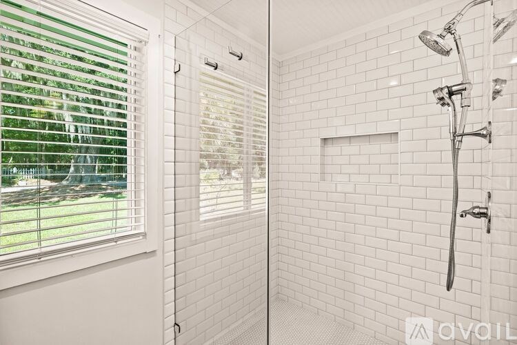 A bathroom with a shower and a window with blinds.